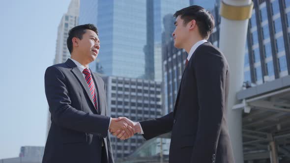 Asian businessmen making handshake after complete the negotiation. Business deal, merger in city.