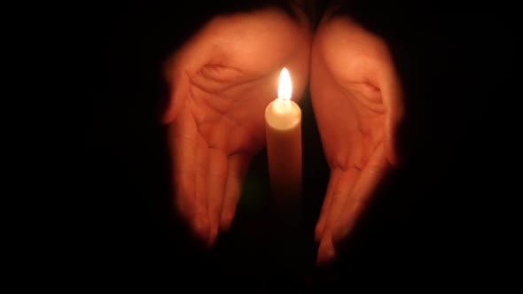 Hands Holding a Burning Candle in Dark
