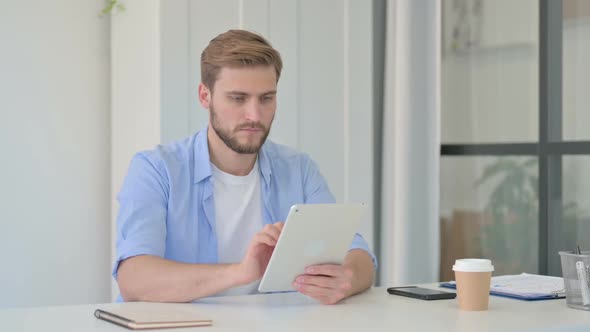 Attractive Young Creative Man Using Tablet in Office