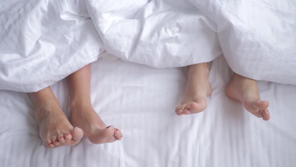 Two Pair of Feet Next To Each Other in a Bed. Mother and Daughter Lie on Bed with White Sheets.