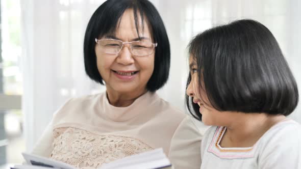 Happy Asian grandmother and lovely girl reading book together.