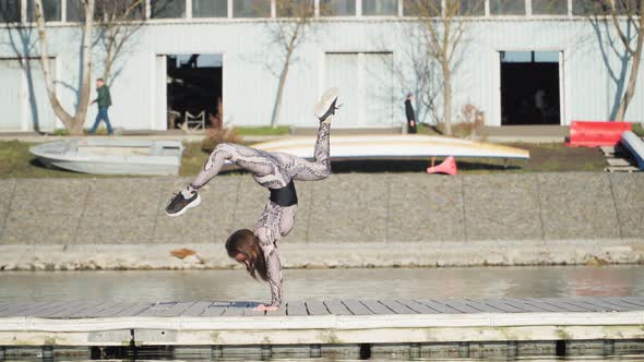 Young Athletic Female Gymnast Performs Handstand Pontoon Near Blue Lake