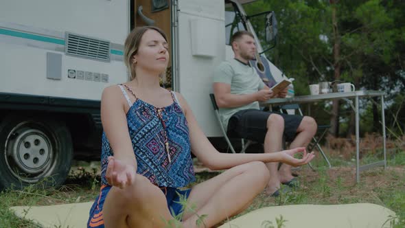 Couple travelling motorhome trip, woman doing yoga meditation and her husband reading book