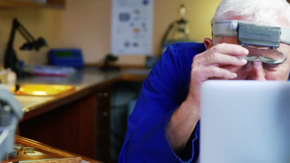 Horologist using laptop while repairing a watch