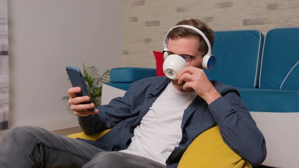 Young Man Listening To Music on Headphones and Drinking a Cup of Coffee.