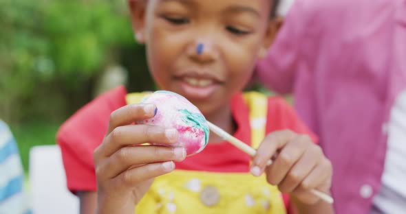 Animation of happy african american girl painting easter eggs in garden