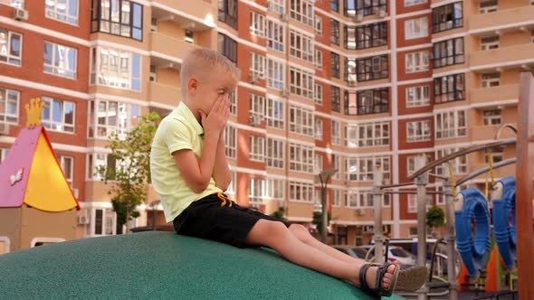 A Little Sad Boy Sits on a Smooth Artificial Stone in a Modern Playground Alone