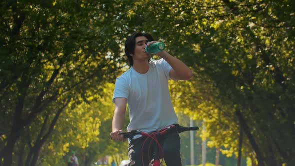 Young Sportive Man Riding a Bike and Drink Water From the Bottle