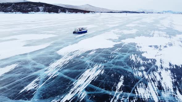 A Hovercraft Rides on the Blue Icy Lake Baikal Covered with White Snow Panoramic Aerial Shot