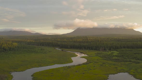 Ascending aerial over spectacular wilderness view meandering river, mountains among clouds backgroun