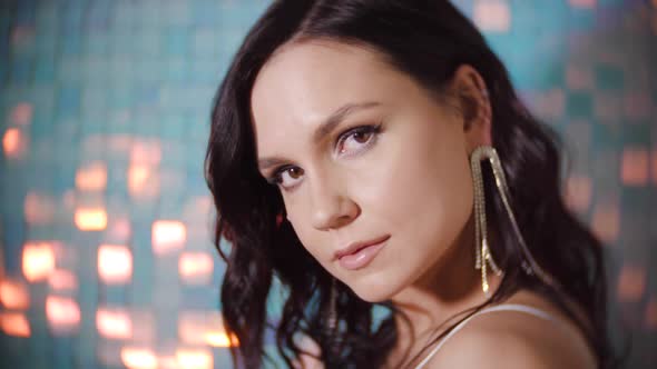 Portrait of a Sexy Brunette Woman with Earrings and a Silver Top on Shiny Background in the Studio