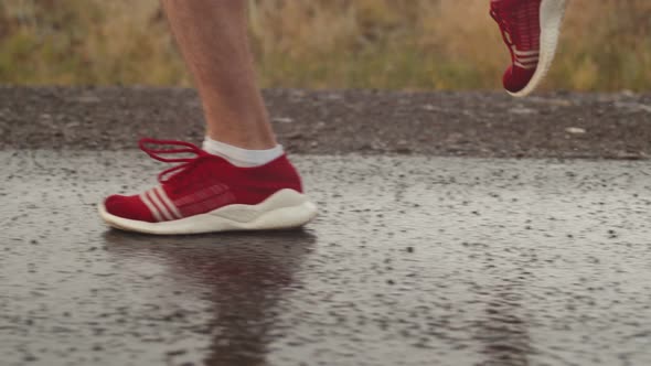 Man Triathlete Legs in Red Sneakers Run on Asphalt During Rain Side View Closeup