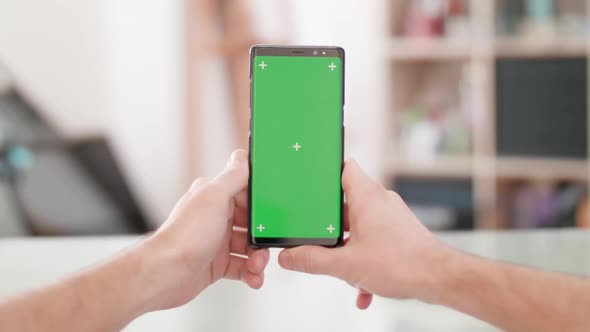 Man s Point of View Holding a Smartphone Vertically with Green Screen on in the Center of the Frame