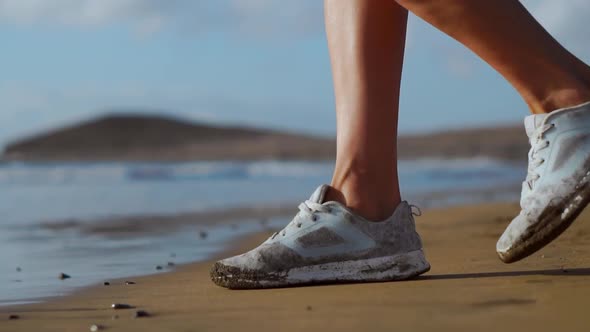 Close-up of the Girl's Feet in Sneakers Fit on the Sand To the Ocean. SLOW MOTION STEADICAM