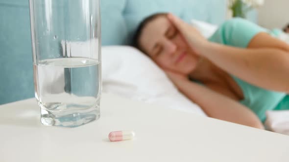 Footage of Young Sick Woman Lying in Bed Taking Pill From Bedside Table and Drinking It with Glass