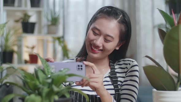 Close Up Of Smiling Asian Woman Holding Smartphone And Taking Photos Of Plants At Home