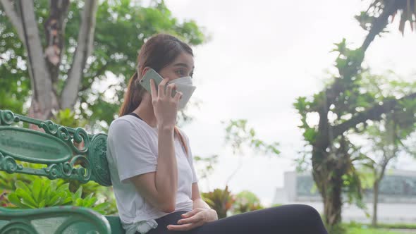 Asian sport woman wear mask, talking on mobile phone in public park.