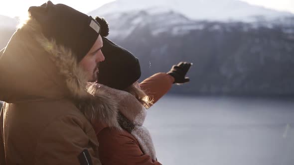 Young Couple in Winter Coats Embracing People Hugging Looking at Stunning View on Lake and Mountains