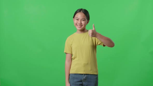 Happy Young Asian Kid Girl Showing Thumbs Up Gesture While Standing In The Green Screen Studio