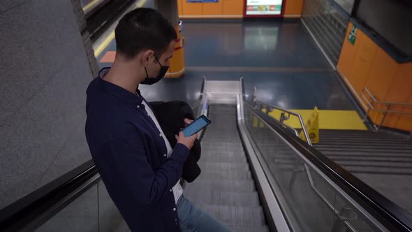 Unrecognizable man surfing internet on smartphone on escalator in underground