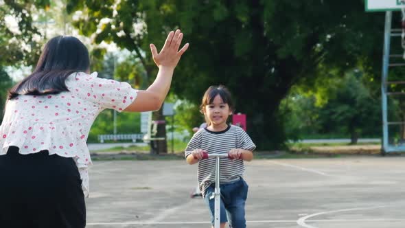 Happy mother and children doing high five while riding scooters in the summer park.