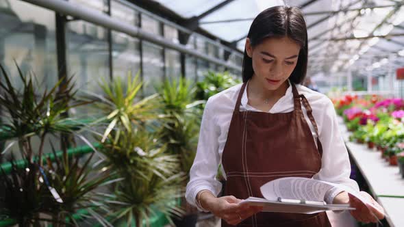 Cheerful florist brunette woman looking at papers and at the camera