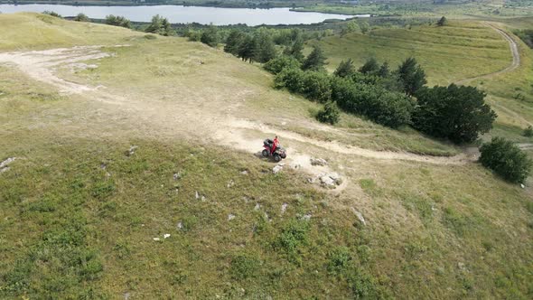 Red ATV with a Driver Stands on the Edge of a Cliff