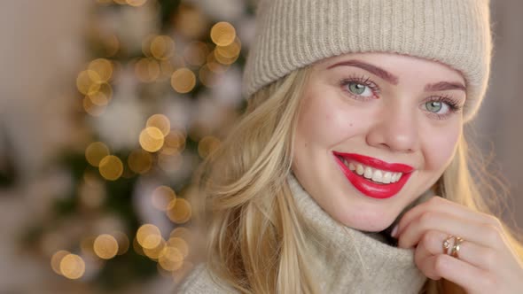 Smiling Blond Woman with Red Lipstick, Dressed in a Warm Woolen Cardigan and Hat Posing in Her Home