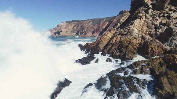 Aerial - Low flying drone along rocky coastline almost gets taken down by splash of massive wave