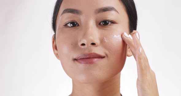 Close Up Portrait of Young Asian Lady Applying Cream on Cheek White Studio Background Slow Motion