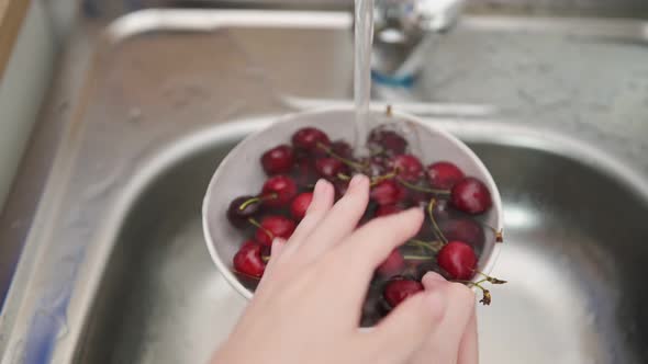 Young woman hands wash cherries in bowl over metal sink