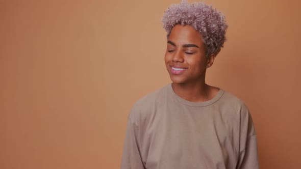 African Woman Looks Gently Aside Stands in Casual Pose Against Brown Background