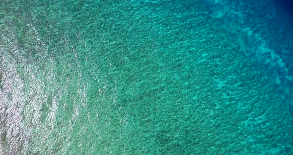 Tropical flying travel shot of a paradise sunny white sand beach and blue water background 