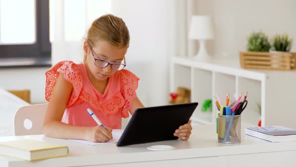Girl with Tablet Pc Writing To Notebook at Home