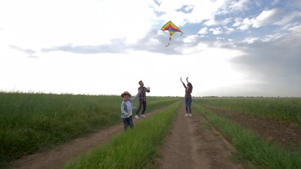 Perfect Family, Child with Kite in Hands Runs Near Young Parents on Countryside on Background of