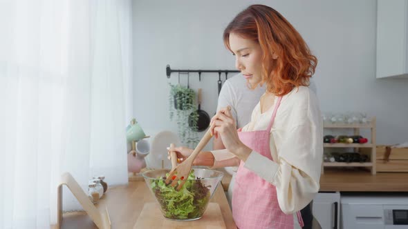 Asian beautiful woman cook green salad with husband eating vegetable healthy food in kitchen at home