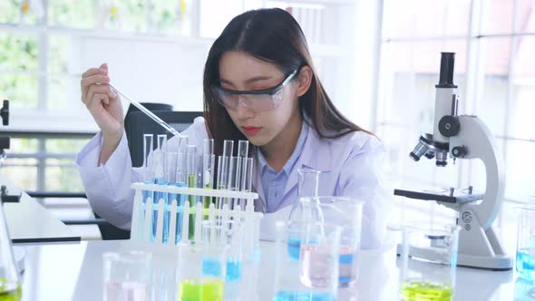 Asian Medical Researcher Working in Pharmacy Laboratory While Mixing Chemical in Flask with Tube