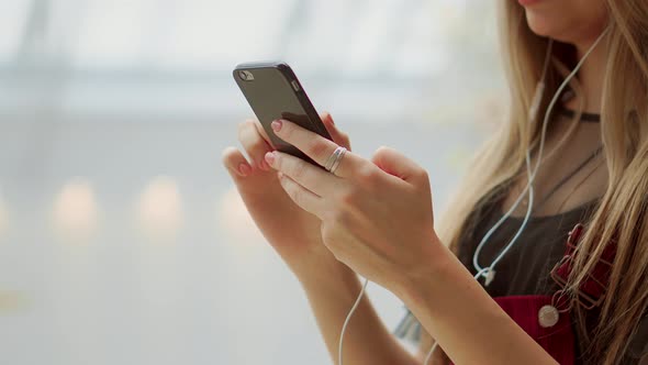 Happy Teenage Girl Holding Bags with Purchases, Smiling While Looking at Phone in Shopping Center