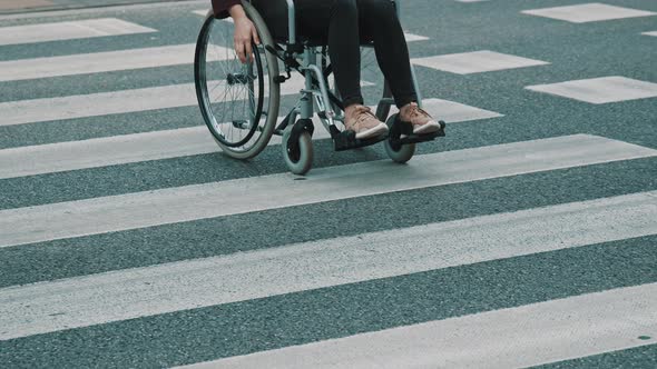 Young Unrecognizable Handicapped Woman in Wheelchair Crossing Street Carefully