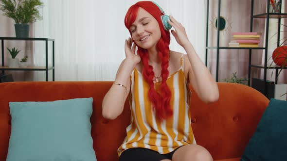 Happy Redhead Girl in Wireless Headphones Dancing Listening Favorite Rock n Roll Music on Home Couch
