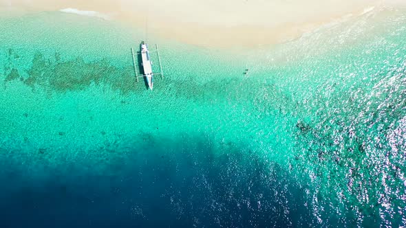 Balinese boat Jukung anchored on shore of tropical island with white sandy beach washed by calm clea