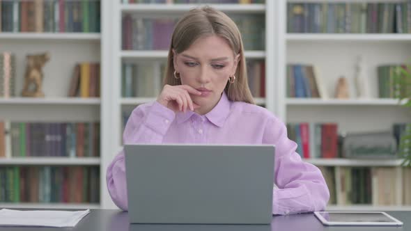 Woman Thinking While Working on Laptop in Office