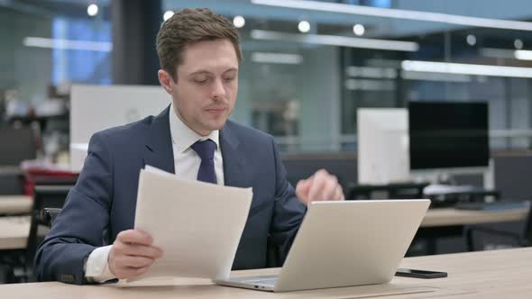 Businessman with Laptop Celebrating Success While Reading Documents