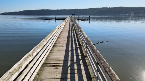 Flying through wood dock pier, danger sign over bright blue water, distant green trees ocean coast