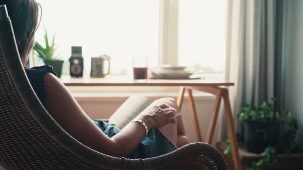 A Woman Reading a Book While Sitting in a Comfortable Wicker Chair