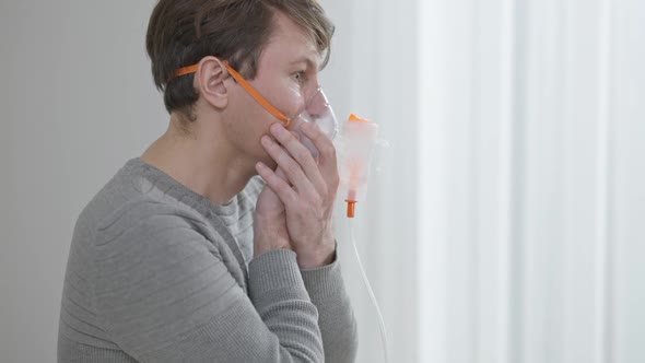 Side View of Concentrated Brunette Caucasian Man Inhaling and Exhaling Using Inhaler