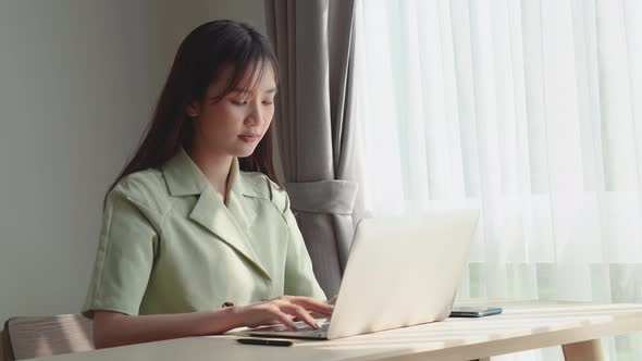 Serious young asian woman working on freelance from home typing email on laptop or study online 
