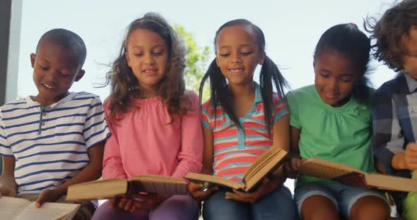 Front view of mixed-race schoolkids reading books in the corridor 4k