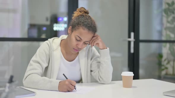 African Woman Thinking While Writing on Paper in Office