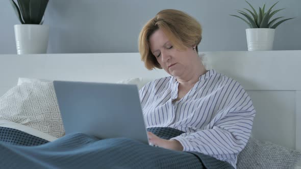 Old Senior Woman Sleeping and Working on Laptop in Bed